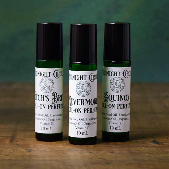 Three bottles of Midnight Circus roll-on perfumes on a wooden surface with a green background.